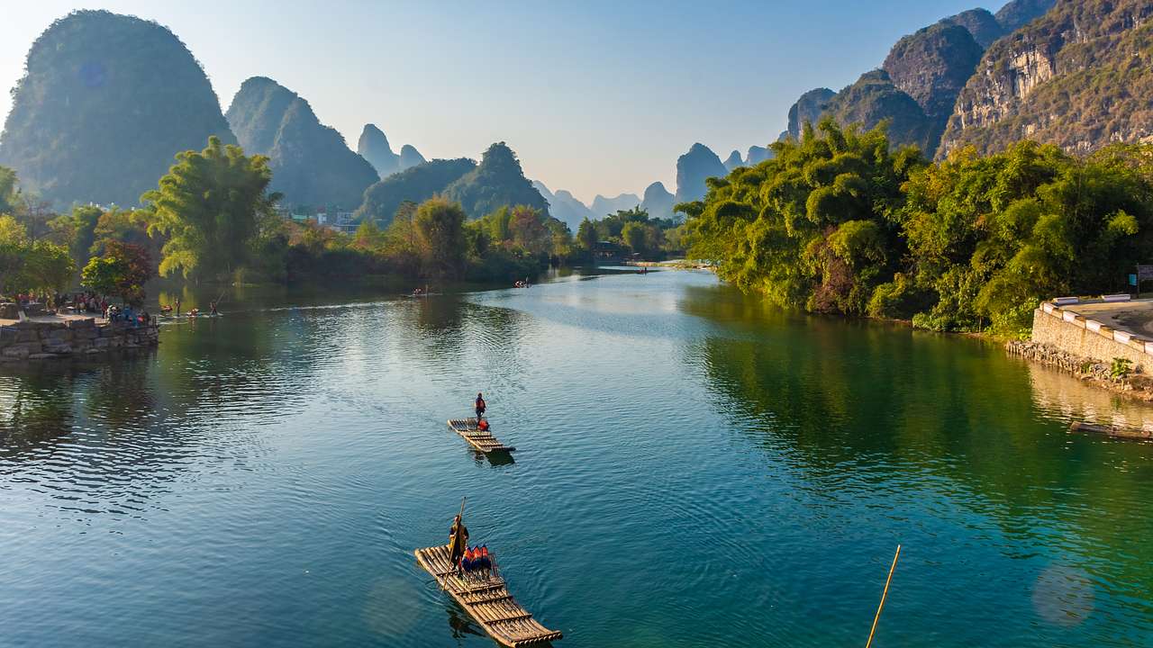 A large river with two bamboo rafts and trees lining up both sides on a nice day