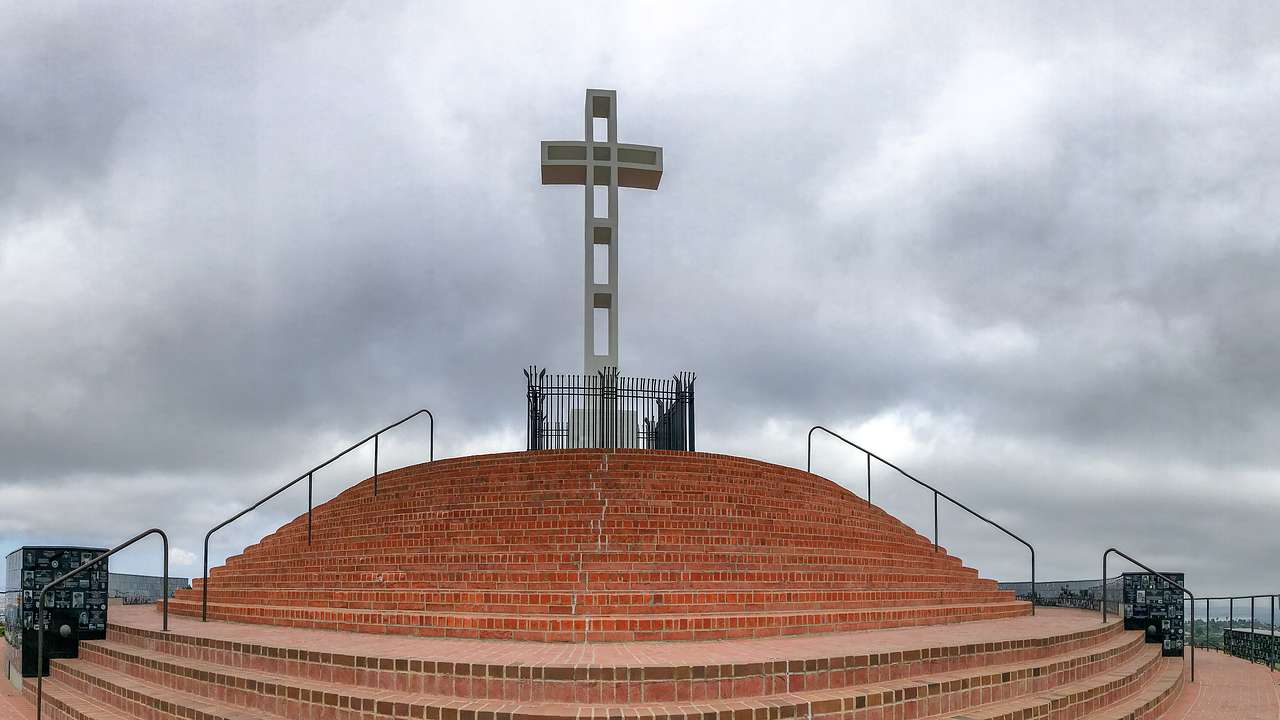 Big cross on top of reddish stairs under a grey, cloudy sky