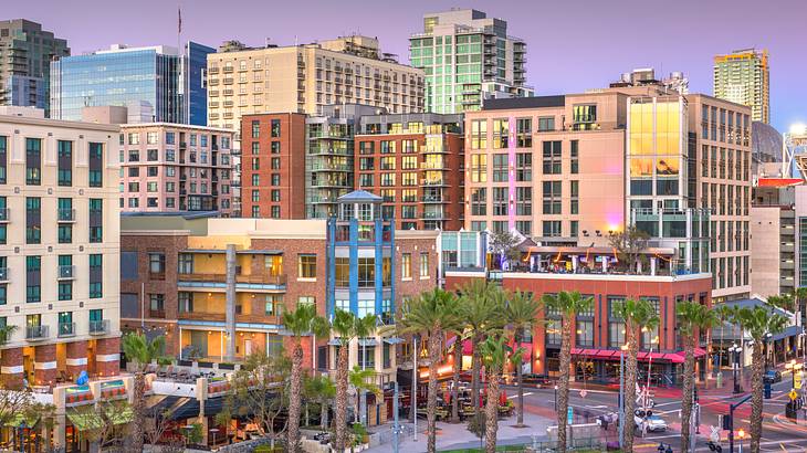 Colorful buildings of different sizes, with trees and a track in front at twilight