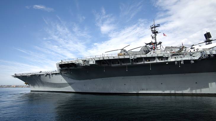 An aircraft carrier with helicopters on top, on a partly cloudy day with water around
