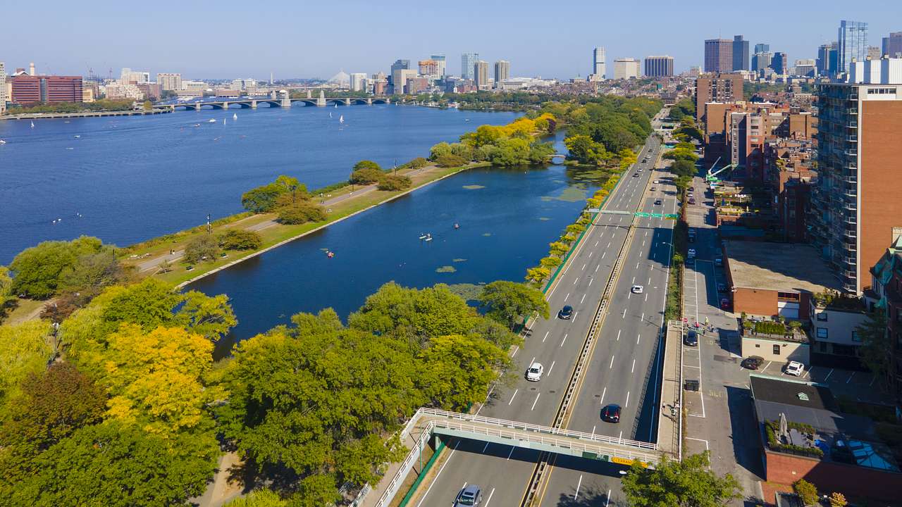 Cars on a highway with buildings on one side and water with trees on the other side
