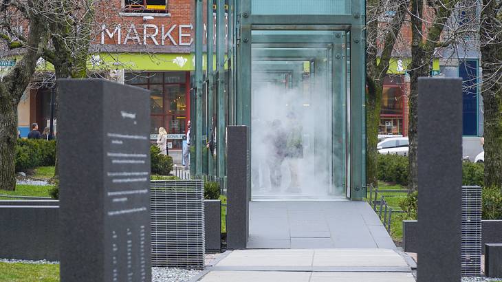 Surrounded by a lawn is a granite pathway with tall glass towers filled with mist