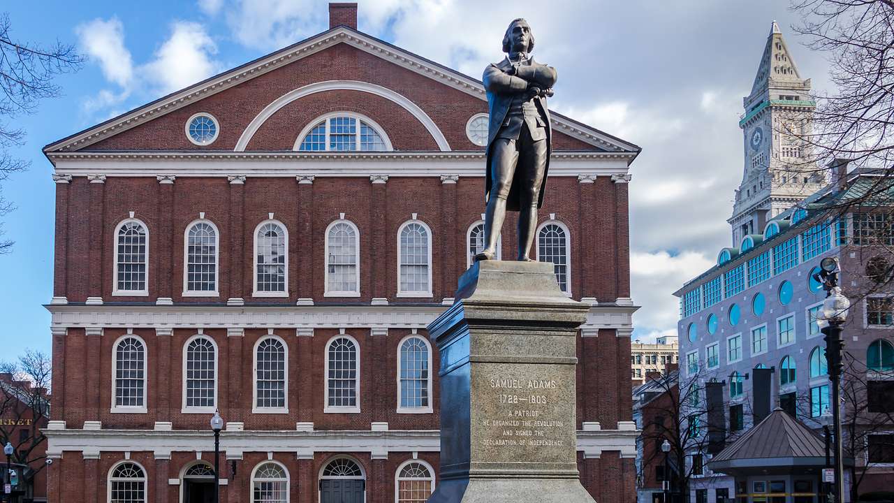 A red-bricked building facing a statue, under a partly cloudy sky