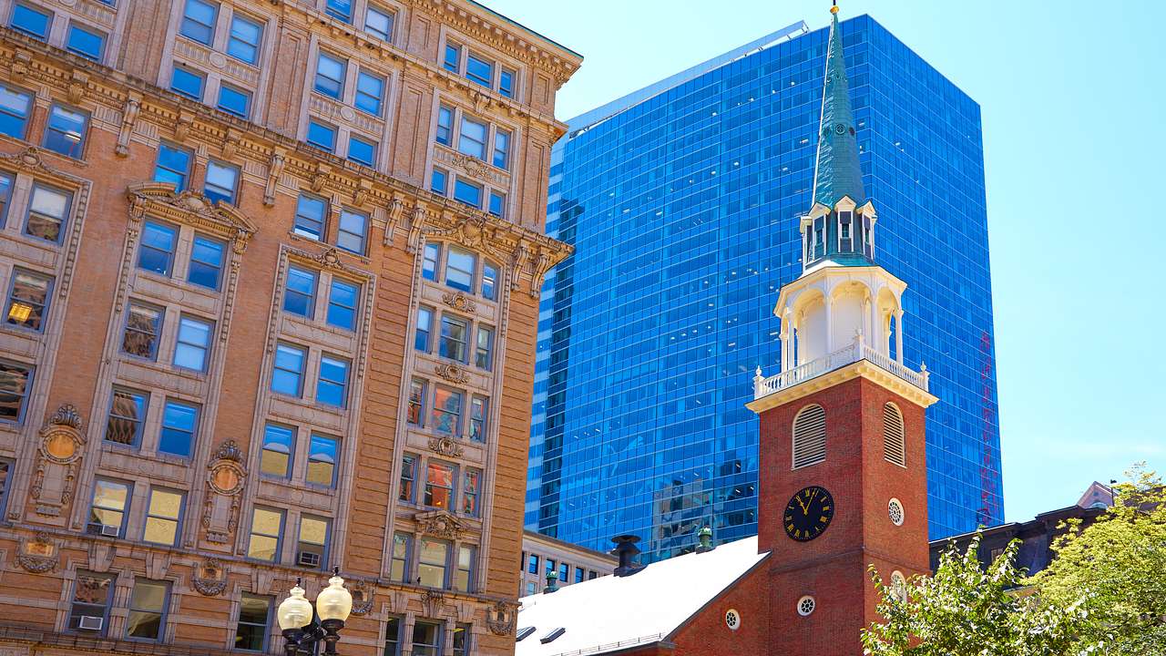 A pointy church top with a tree on the right and buildings behind on a nice day