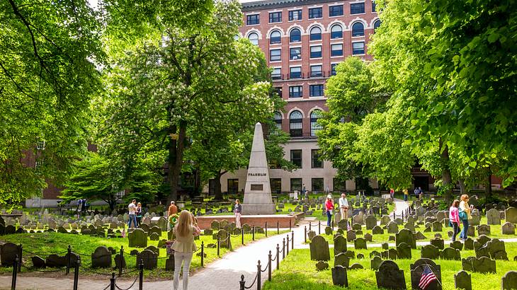 A path and obelisk in the middle, with tombstones and green grass and trees around