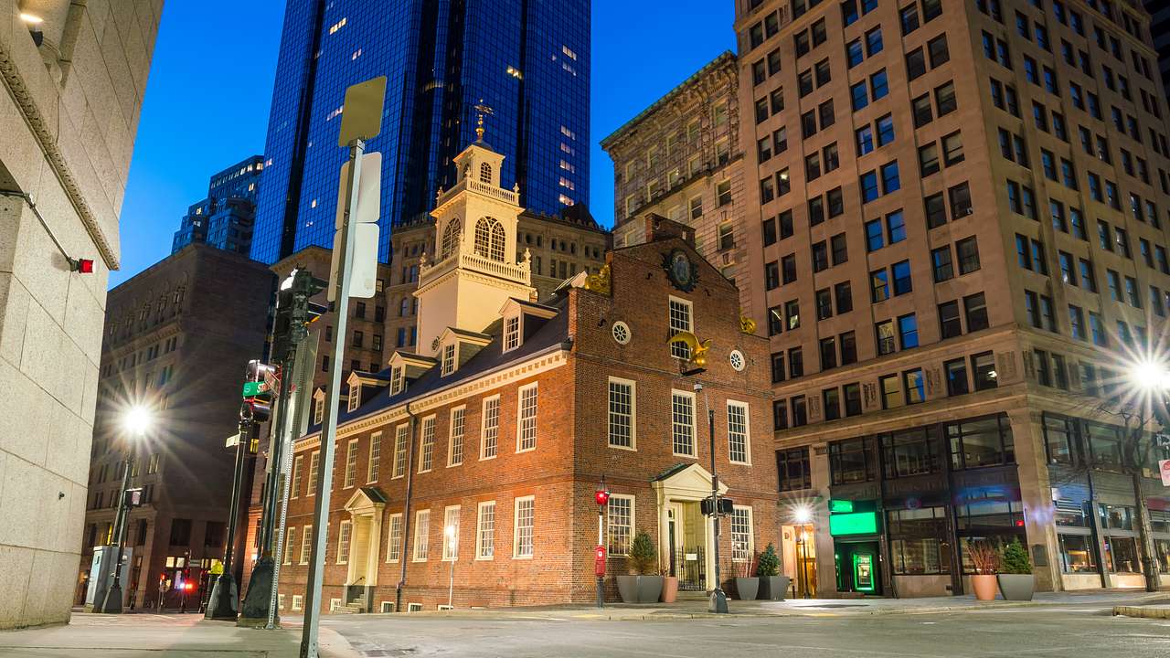 A historic building with a tower at an intersection, surrounded by modern buildings