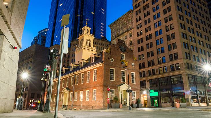 A historic building with a tower at an intersection, surrounded by modern buildings