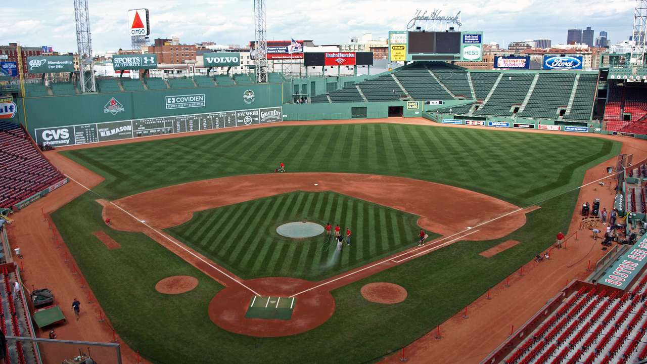 Baseball stadium with landscaped green grass, dirt paths, and a green wall behind