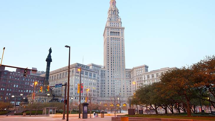 An urban square with trees, and a pointy tower and a statue in the background