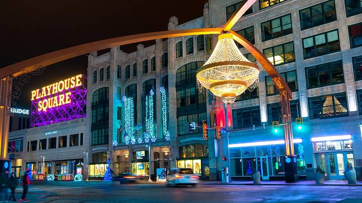 A street at night with a neon sign saying "Playhouse Square" and a lit-up chandelier