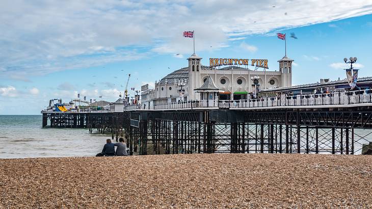 A very long pier above a rocky beach and water, with a domed building at the back