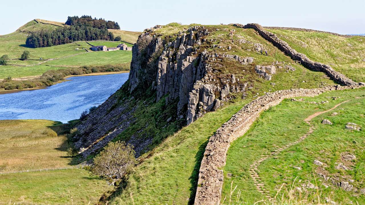 Ancient wall leading up a steep, rocky green hill, overlooking a body of water