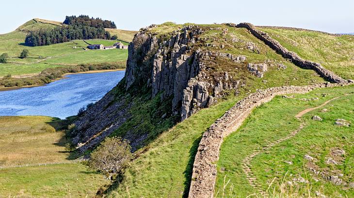 Ancient wall leading up a steep, rocky green hill, overlooking a body of water
