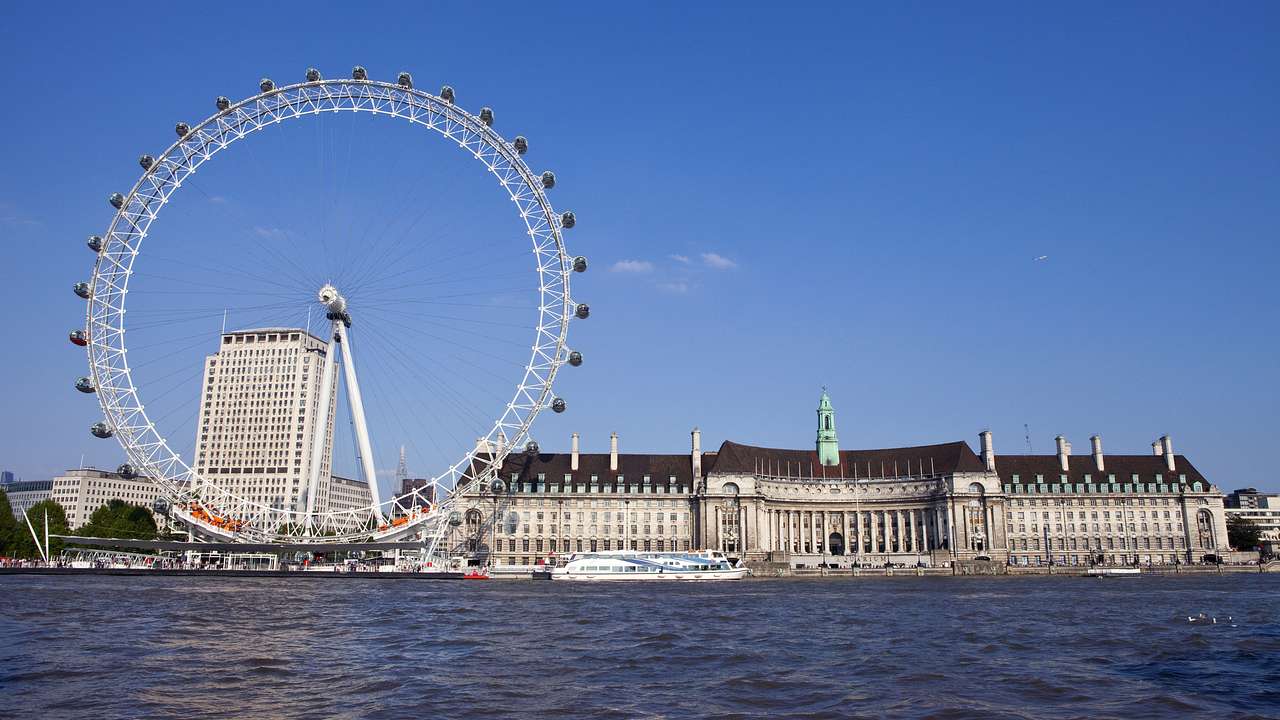 An observation wheel along water, with a rectangular building on the right