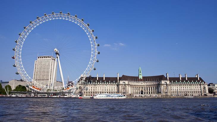 An observation wheel along water, with a rectangular building on the right