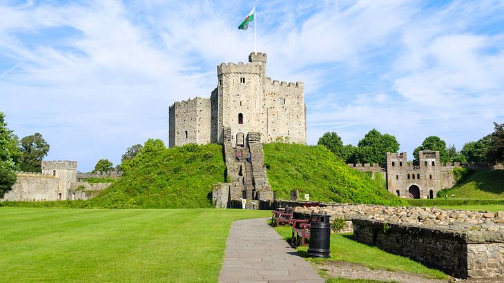 A staircase leading up to a stone castle on top of a green hill, with a flag on top