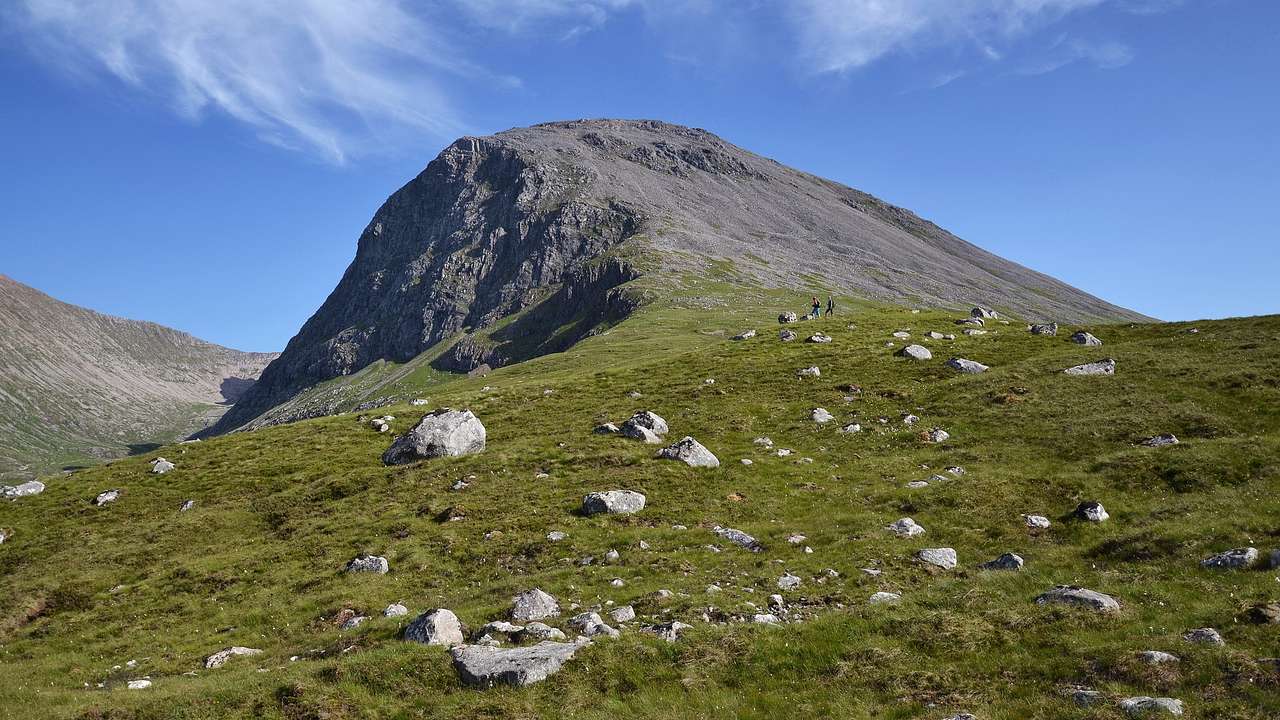 A grassy hill with rocks and a mountain in the background on a sunny day