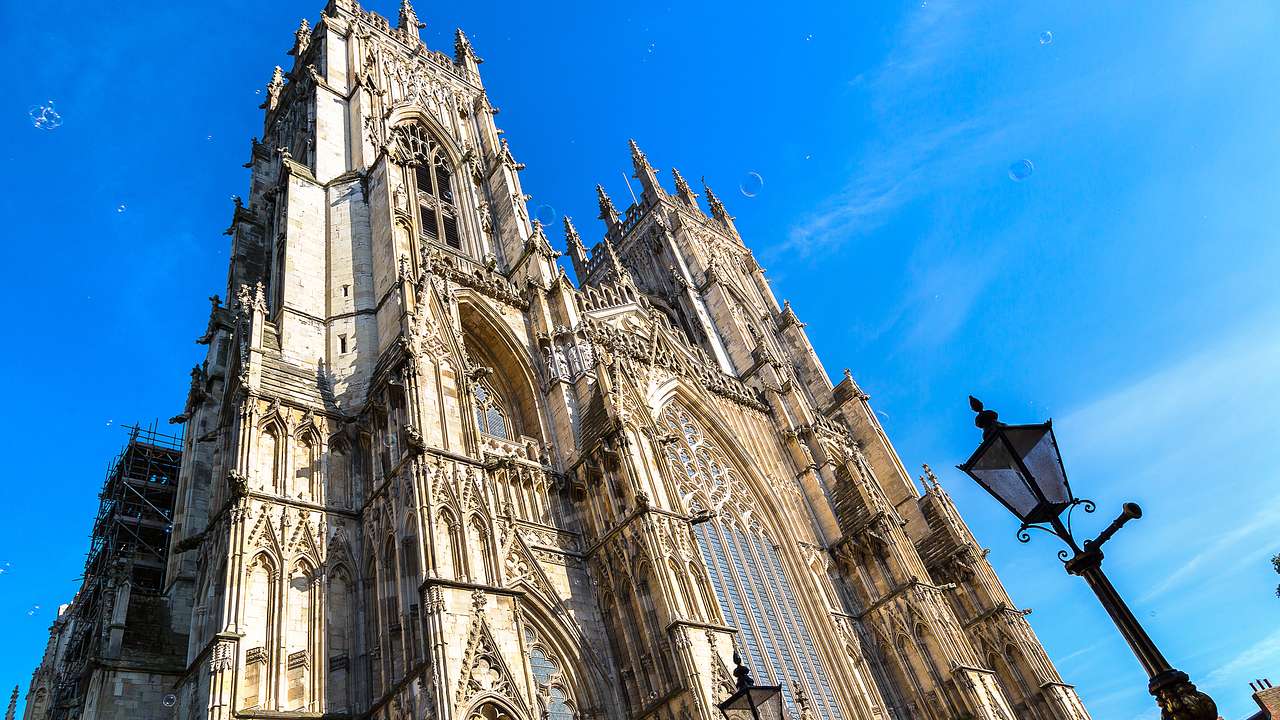 Two tall tower tops of a cathedral with a lamppost below, against a blue sky