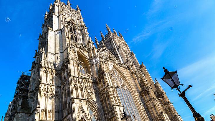 Two tall tower tops of a cathedral with a lamppost below, against a blue sky