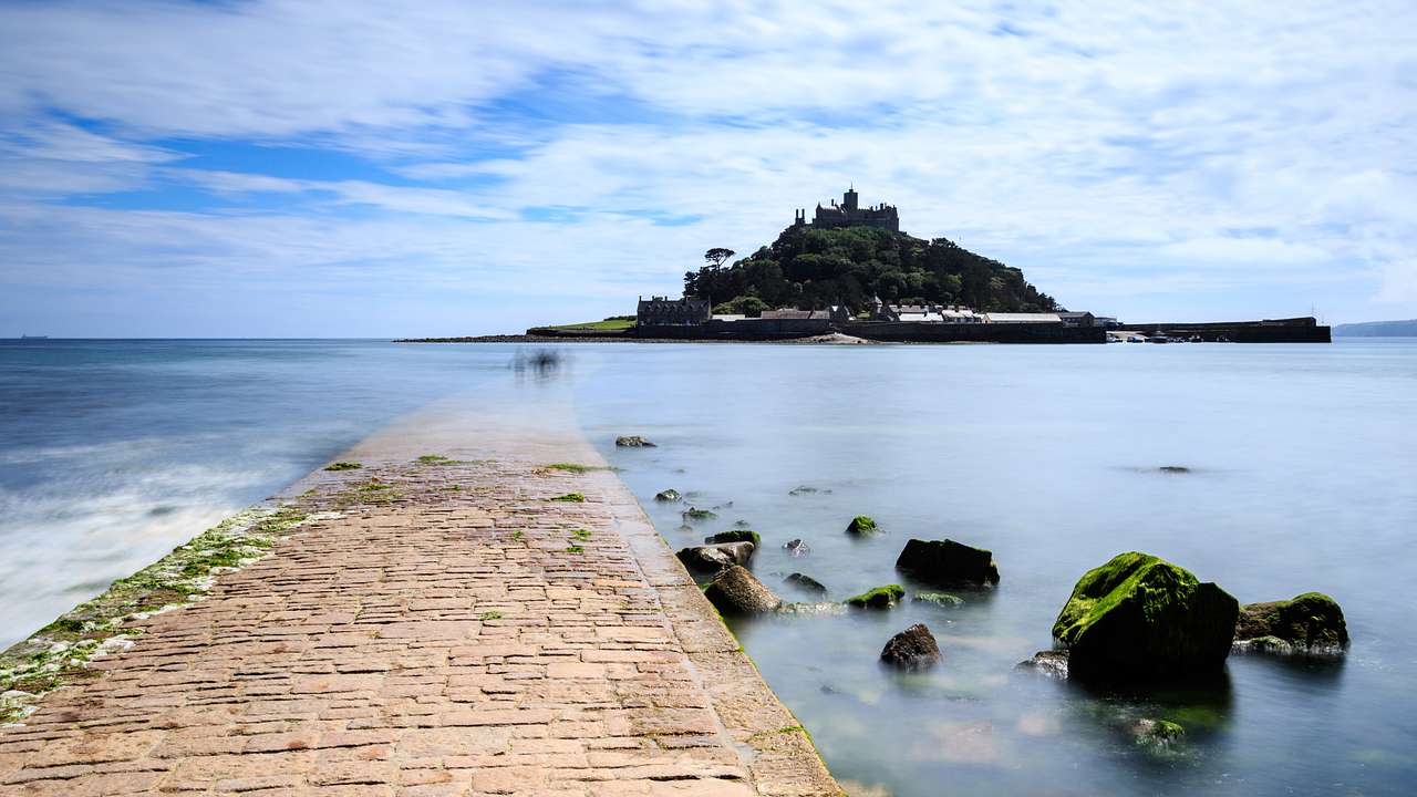 A tree-filled island with a castle on top of the hill, across a shallow body of water