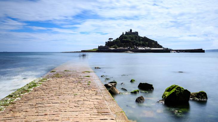 A tree-filled island with a castle on top of the hill, across a shallow body of water