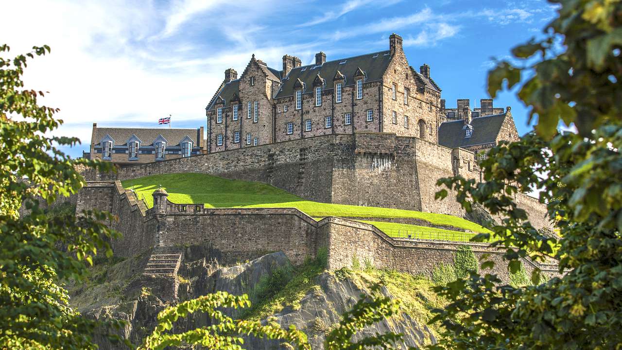 A view of a castle on a hill surrounded by green trees from below