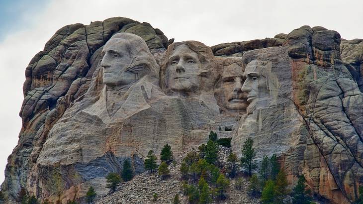 A grey rocky mountain with four large man faces carved into it
