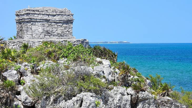 Old Mayan ruins atop a rocky cliff overlooking vast blue water