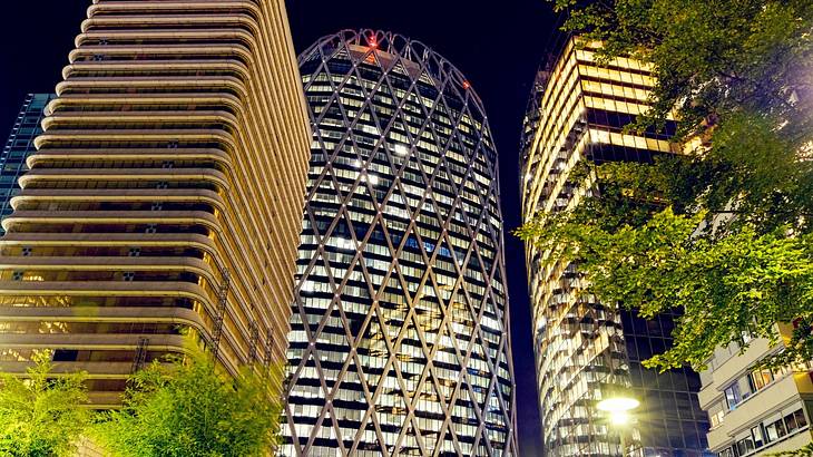 Tall lit up glass buildings with a street light and trees in front at night