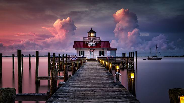 A lighthouse at the end of a pier at sunrise with boats around