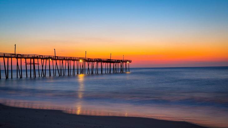 Colorful sunrise view of Rodanthe Pier over water from the shore