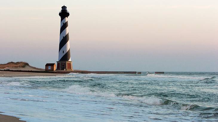 A black and white candy cane design lighthouse along a coastline