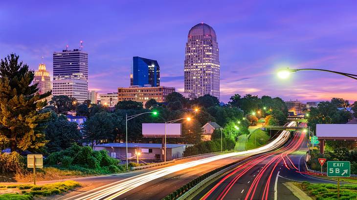 A highway with cars zooming by, leading to a city skyline at dusk A highway with cars zooming by, leading to a city skyline at dusk