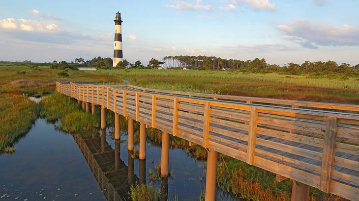 A lighthouse at the end of a long walkway, surrounded by marshland