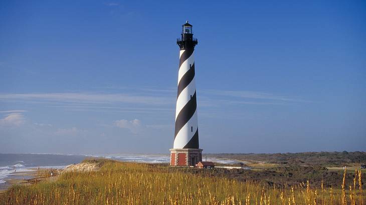 A black and white striped lighthouse overlooking the sea with sea grass around