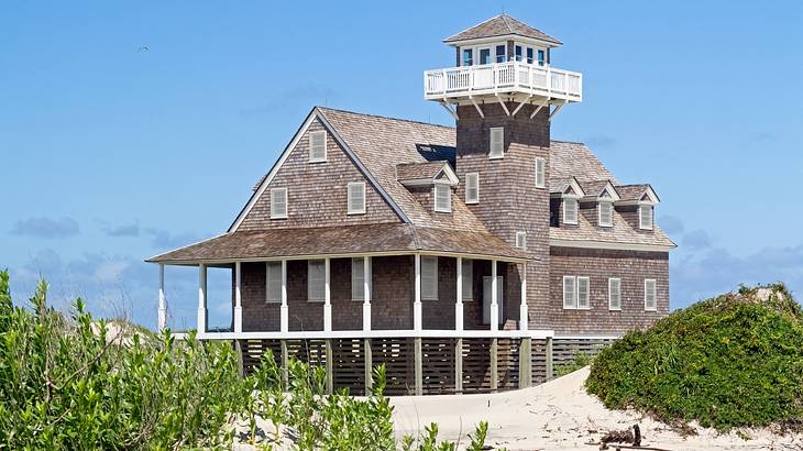 A brown building with a tower, surrounded by blue sky, sand dunes and bushes