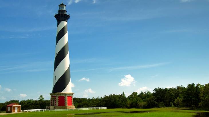 Black and white striped lighthouse standing tall against blue sky on a green field