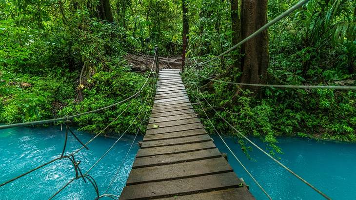 Wooden hanging bridge over a beautiful turquoise river in a green forest