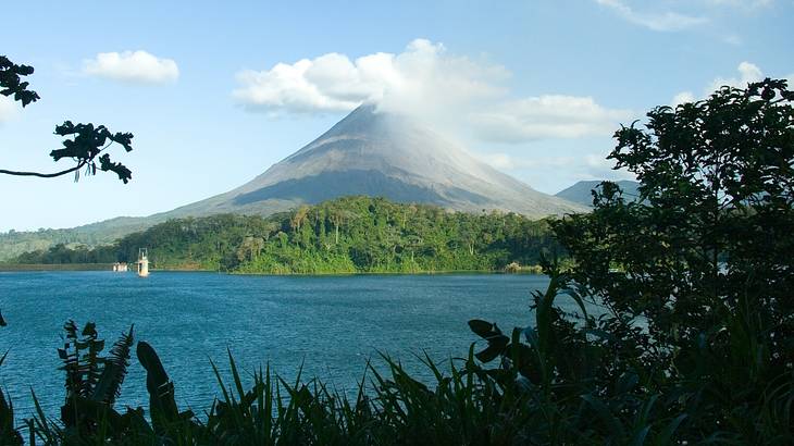 View of a volcano from behind a lake, rising from a rainforest