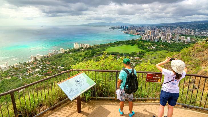 Tourists enjoying a panoramic city and coastline view from a green mountain top
