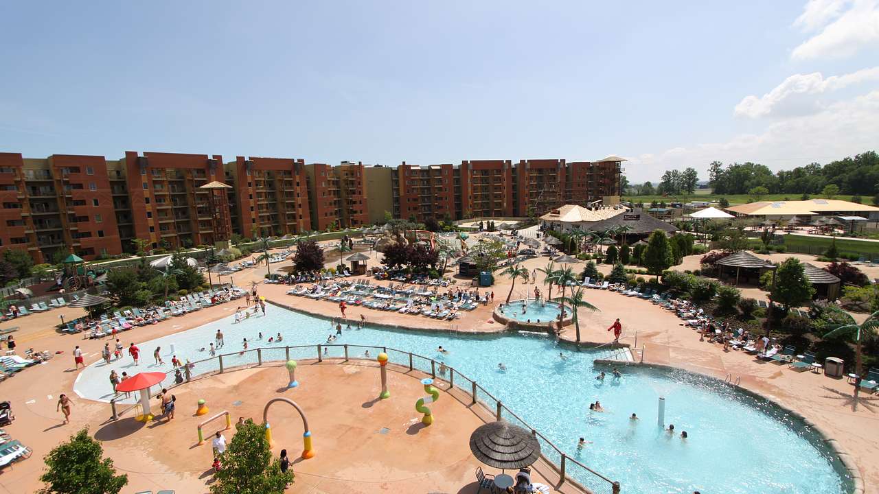 An aerial view of a large outdoor pool with people in it and buildings at the back