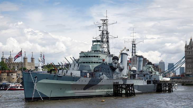 A side view of a long navy boat floating on a river with Tower Bridge at the back A side view of a long navy boat floating on a river with Tower Bridge at the back