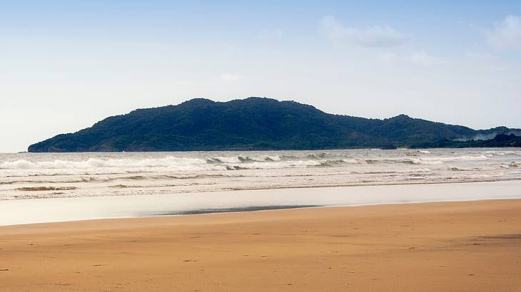Waves breaking on a sandy orange beach with mountains in the distance