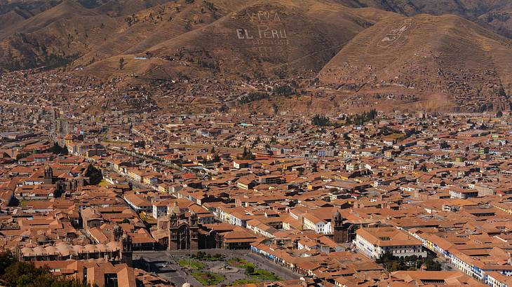 An aerial photo of the brown rooftops of Cusco City with dry hills behind