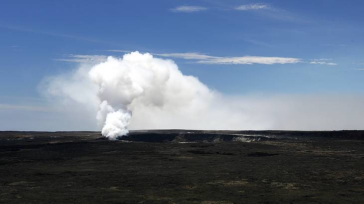 White smoke coming out of a vent in a black volcano against a blue sky