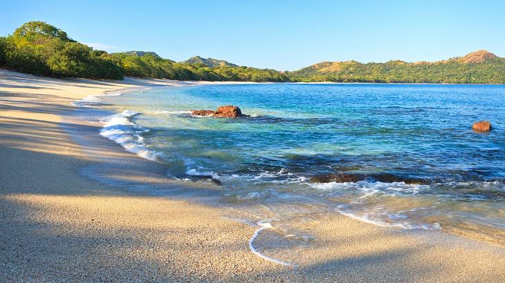 Waves crashing on a sandy beach with seashells and mountains in the background Waves crashing on a sandy beach with seashells and mountains in the background