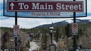 A red sign that says "To Main Street" with a mountain, trees and a town behind it