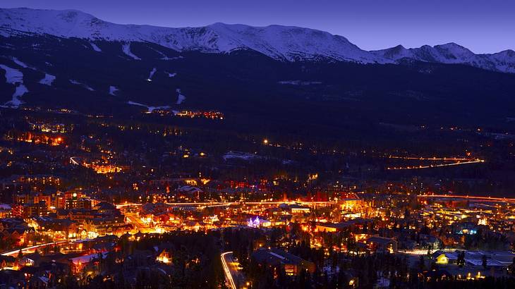 Aerial of homes lit up at night with dark snow-capped mountains in the back
