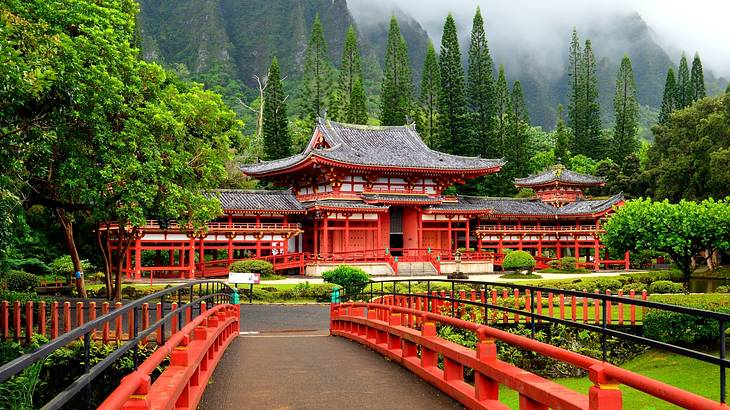 View from a bridge of a red Chinese temple at the foot of a mountain with fog on top View from a bridge of a red Chinese temple at the foot of a mountain with fog on top