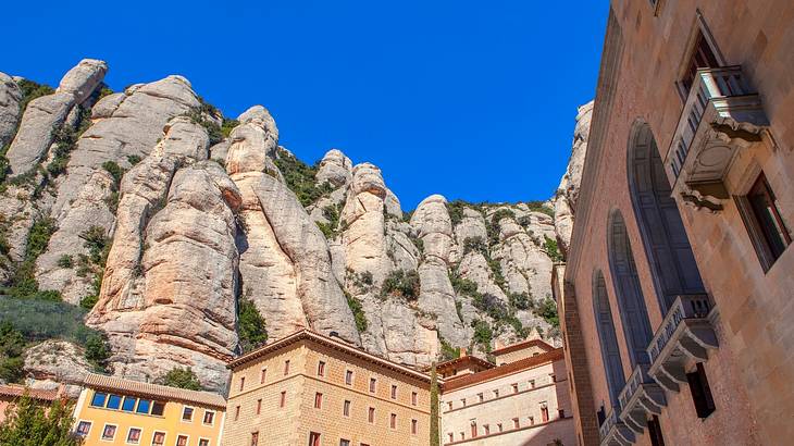 Looking up at monastery buildings against tall rockface and blue sky